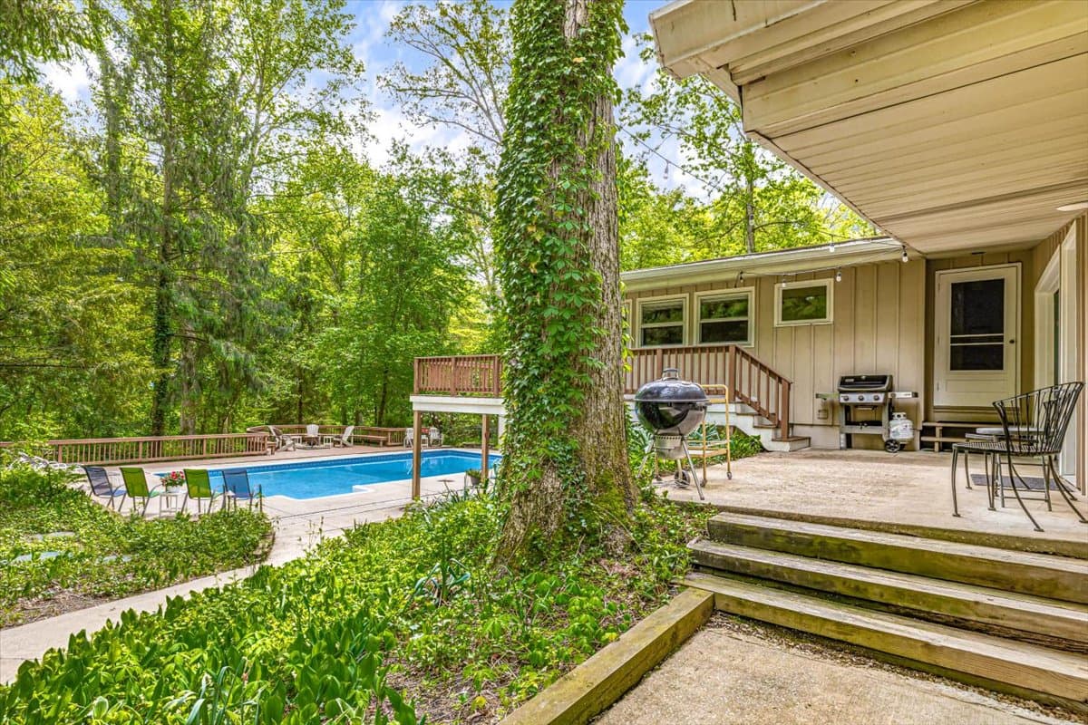 Private swimming pool with patio furniture and wooded backdrop